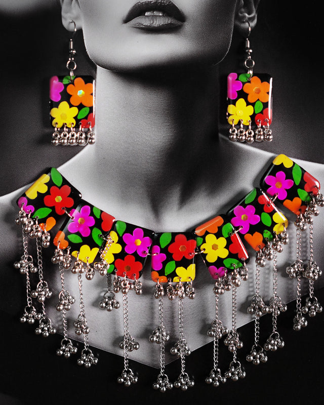 A close-up of the model wearing the Parizad floral jewelry set, showing the colorful hand-painted flowers on a black base. The silver gungroo details add a soft, playful charm, while the vibrant design brightens up the neckline — Muselot.