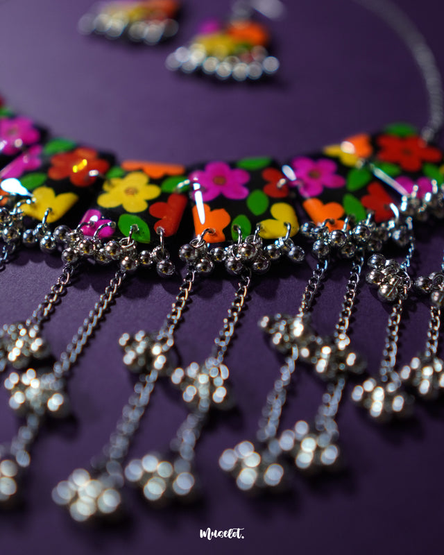 A close-up shot of the Parizad floral jewelry set highlighting the delicate silver chains and gungroo drops that sway gently below the colorful floral tiles. The detailing adds a playful jingle and elevates the charm of this handcrafted statement piece — Muselot.