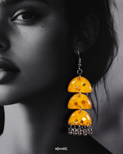 A close-up of a woman wearing Parvaaz handmade yellow drop earrings, highlighting their vibrant yellow tones and smooth, glossy finish. The delicate metallic chains add movement and charm, showcasing a bold and cheerful accessory perfect for statement styling — Muselot.