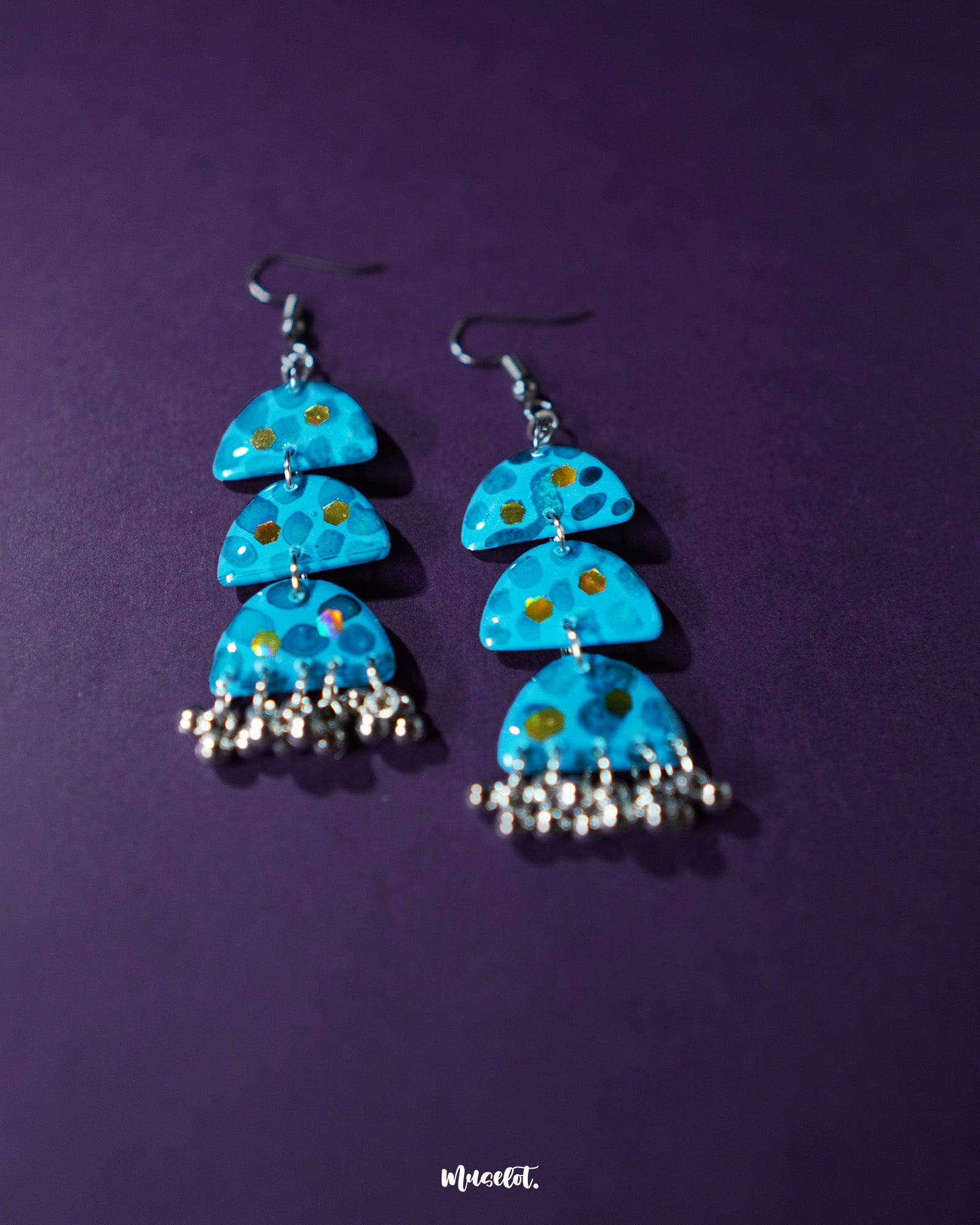Parvaaz blue drop earrings displayed against a purple background, showcasing their hand-painted floral details and highlighting the vivid contrast and artistic craftsmanship — Muselot.