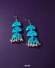 Parvaaz blue drop earrings displayed against a purple background, showcasing their hand-painted floral details and highlighting the vivid contrast and artistic craftsmanship — Muselot.