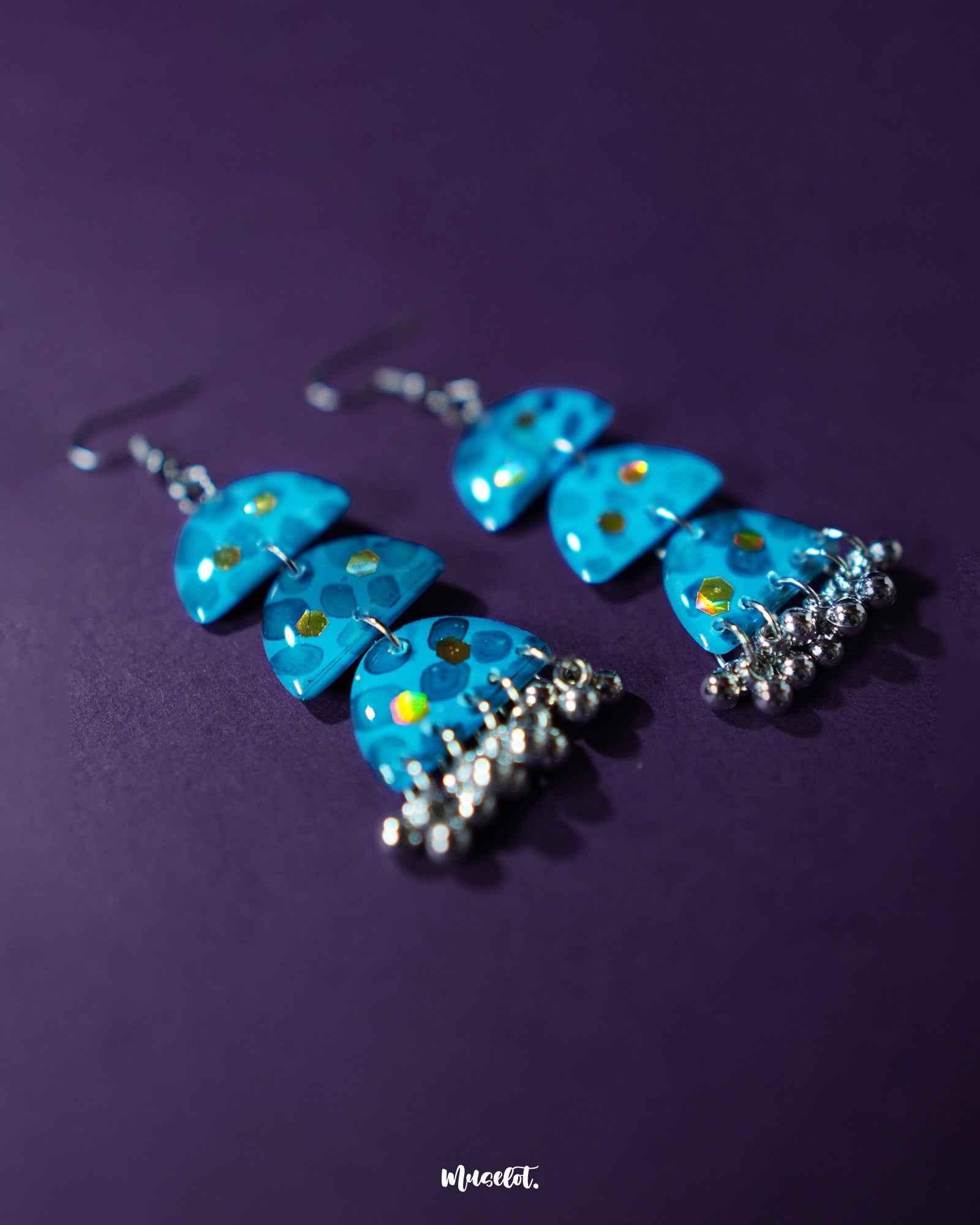 A pair of Parvaaz blue drop earrings displayed on a soft purple background, showcasing their vivid hand-painted blue floral design and elegant drop silhouette that reflects traditional craftsmanship with a modern charm — Muselot.