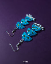 Close-up of Parvaaz blue drop earrings featuring intricately hand-painted floral patterns in shades of blue with delicate leaf accents, highlighting the fine detailing and showcasing the charm of artisanal jewelry — Muselot.