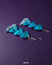 A detailed shot of Parvaaz blue drop earrings, displaying a rich blend of blue floral motifs and subtle leafy accents, highlighting the handcrafted charm and showcasing elegant traditional craftsmanship — Muselot.