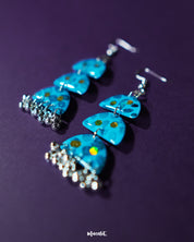 Close-up view of Parvaaz blue drop earrings featuring hand-painted blue flowers with delicate green leaves, highlighting their artistic finesse and showcasing a graceful blend of traditional and modern design — Muselot.