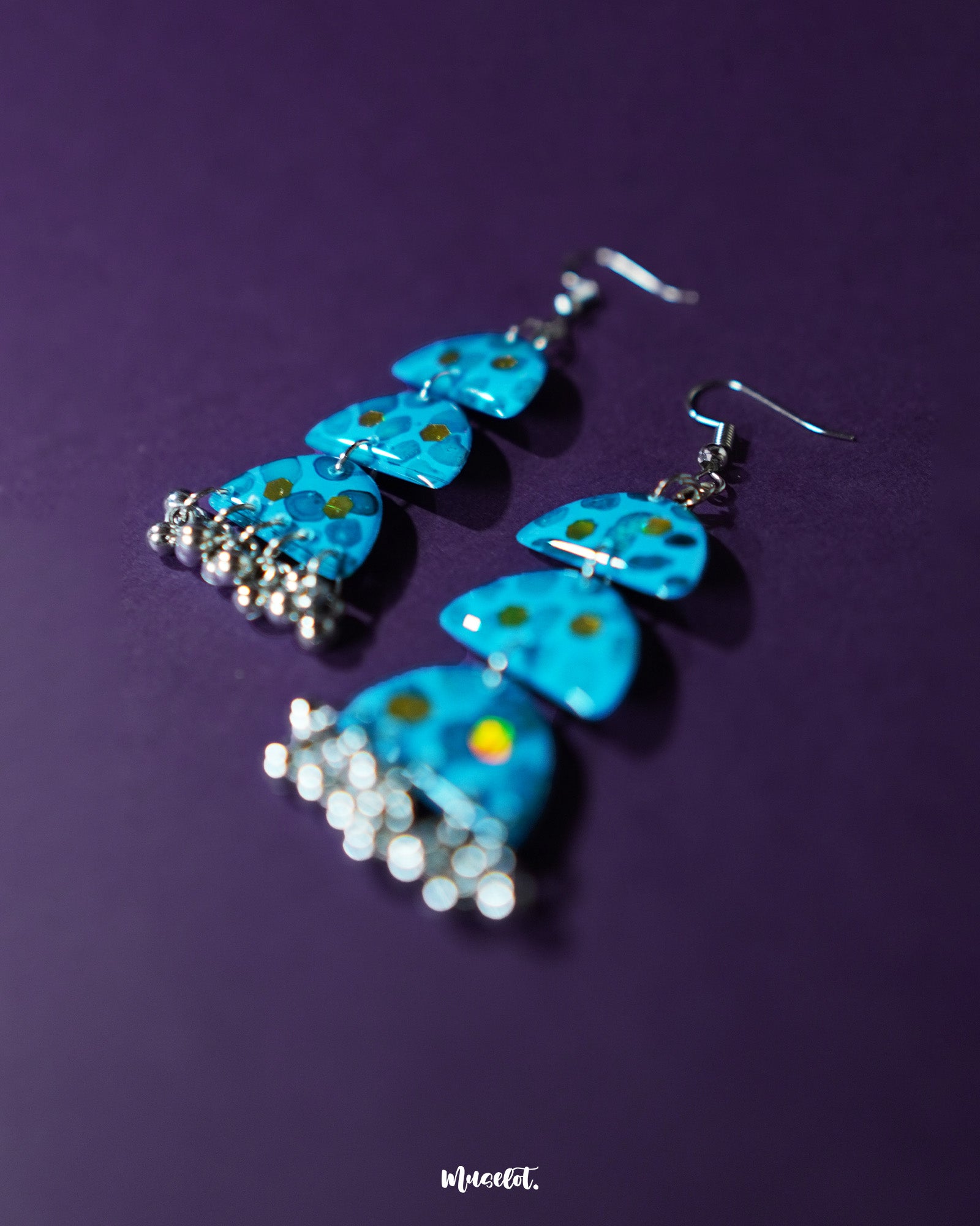 Parvaaz blue drop earrings laid out against a soft purple background, showcasing the hand-painted floral details in shades of blue and green that highlight their artisanal charm and delicate craftsmanship — Muselot.