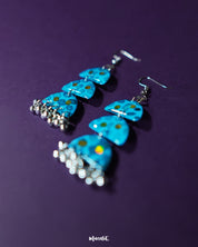 Parvaaz blue drop earrings laid out against a soft purple background, showcasing the hand-painted floral details in shades of blue and green that highlight their artisanal charm and delicate craftsmanship — Muselot.