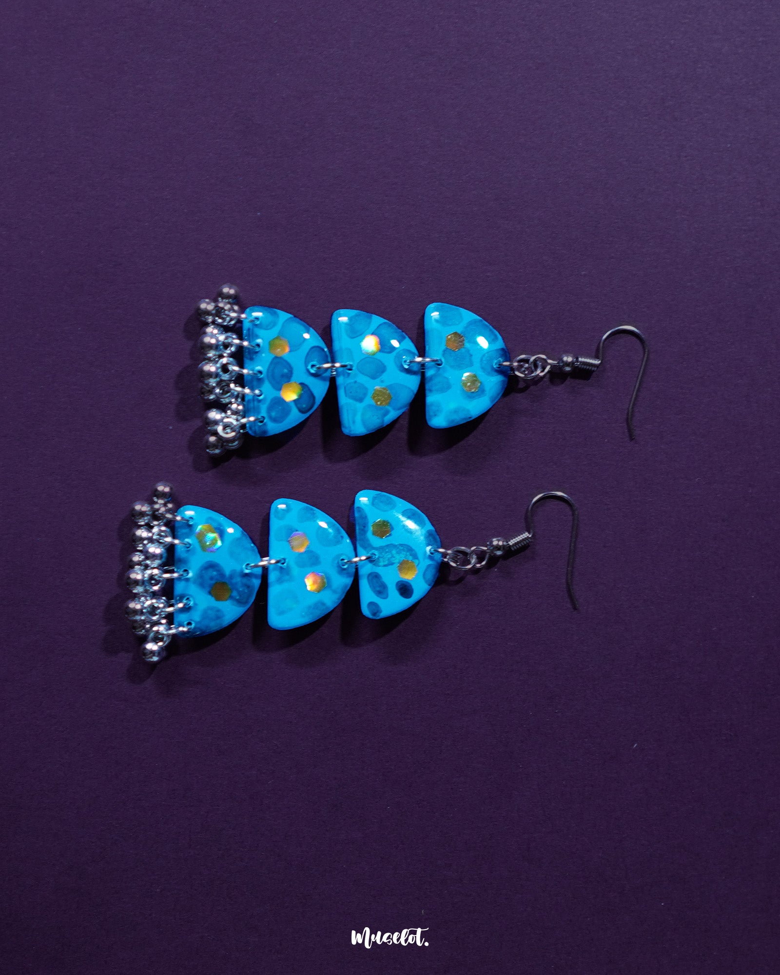 Parvaaz blue drop earrings featuring intricate floral motifs in cool tones of blue and hints of green, highlighting the graceful design and showcasing the fusion of delicate art with bold accessory aesthetics — Muselot.