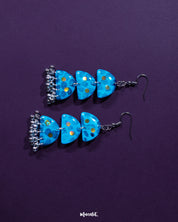Parvaaz blue drop earrings featuring intricate floral motifs in cool tones of blue and hints of green, highlighting the graceful design and showcasing the fusion of delicate art with bold accessory aesthetics — Muselot.