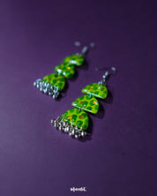 A pair of Parvaaz green drop earrings placed against a soft purple background, showcasing the elegant shape and subtle dark green dotted on a light green base detailing that add a touch of earthy grace — Muselot.