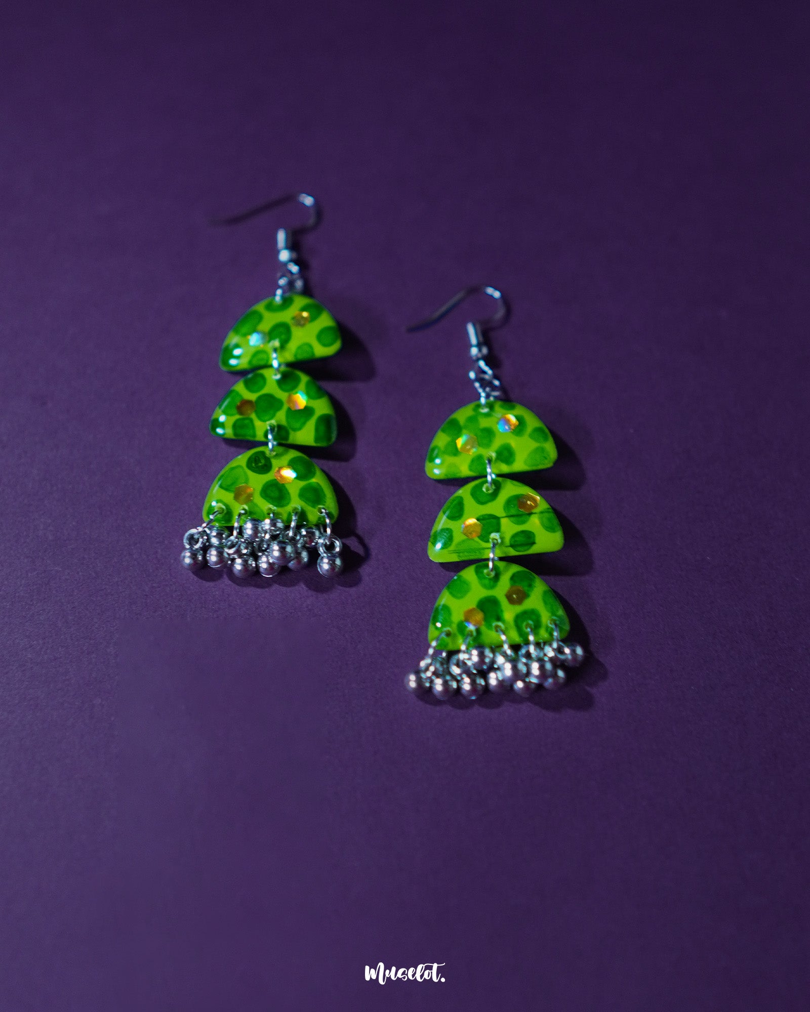 A close-up of Parvaaz green drop earrings placed on a soft green backdrop, highlighting the deep green dotted detailing and curved drop shape, showcasing the handmade artistry and a grounded, nature-inspired charm — Muselot.
