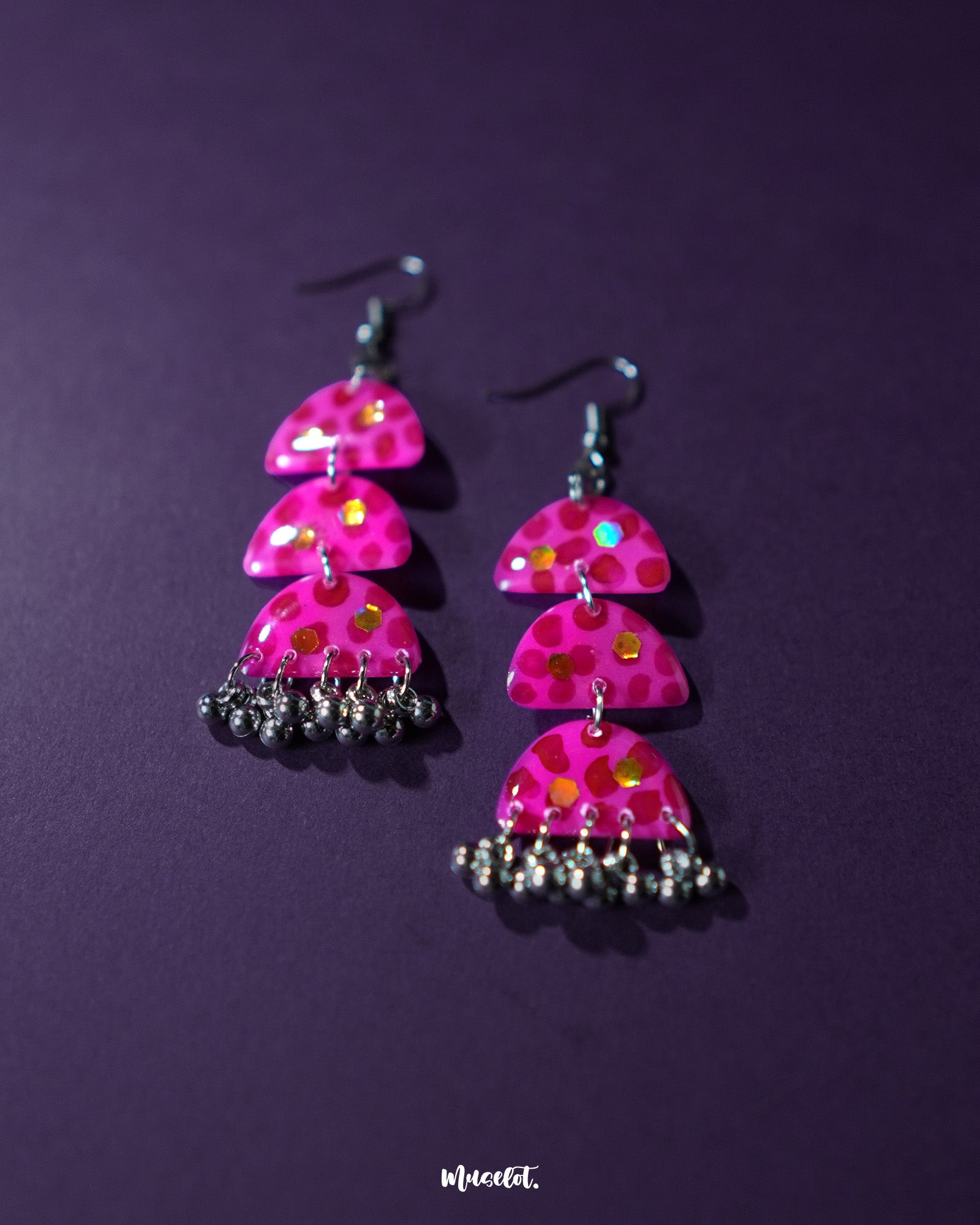 A pair of Parvaaz pink drop earrings displayed against a soft purple backdrop, highlighting the delicate floral motifs and showcasing their handcrafted detailing and graceful silhouette — Muselot.