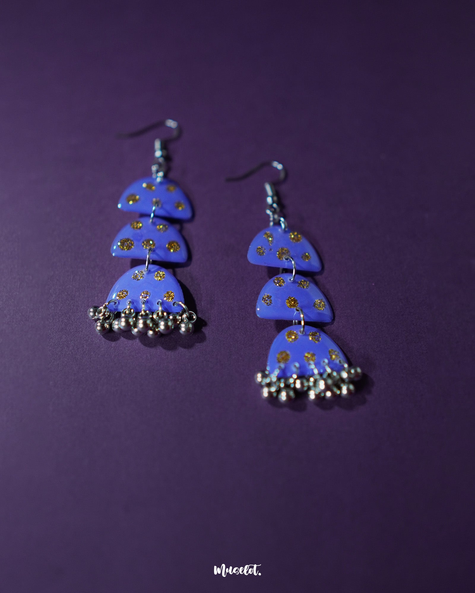 Parvaaz purple drop earrings displayed on a soft neutral surface, showcasing their handcrafted finish and shimmering golden dot accents that add a subtle festive flair — Muselot.