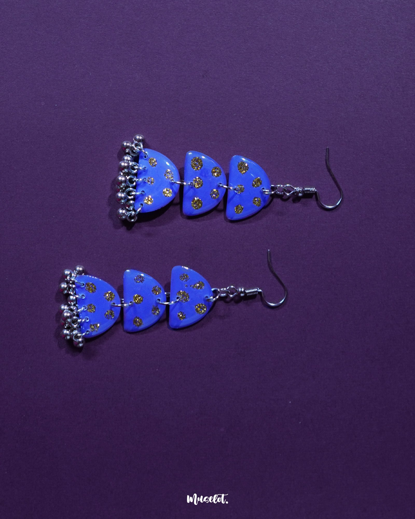 A pair of Parvaaz purple drop earrings placed against a soft background, highlighting their teardrop shape and the intricate golden dot accents that showcase handcrafted detail and refined charm — Muselot.