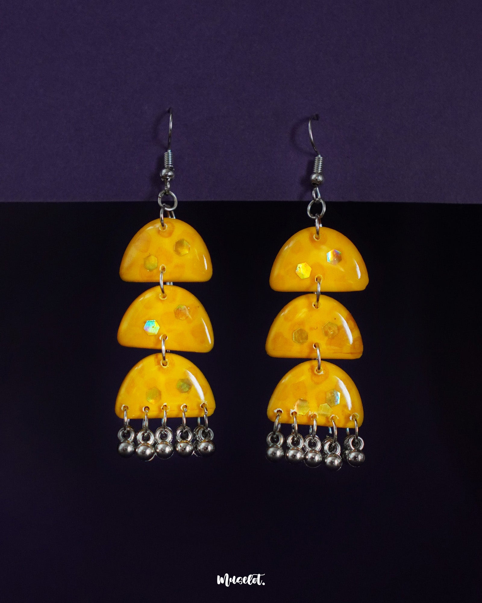 Parvaaz yellow drop earrings set against a deep purple background, featuring glossy hand-painted yellow domes with playful green accents and metallic danglers, highlighting vibrant energy and showcasing joyful craftsmanship — Muselot.