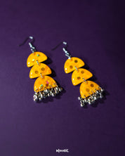 A pair of Parvaaz yellow drop earrings placed against a soft purple background, highlighting their vibrant floral design and showcasing the delicate handcrafted details that bring a playful charm — Muselot.