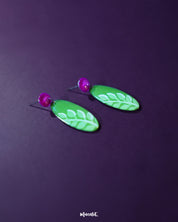  The Patbaan drop earrings featuring delicate hand-painted white leaf motifs on an oval green base, paired with bold pink studs for a lively, nature-inspired statement — Muselot.