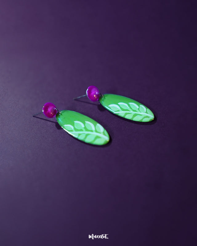  The Patbaan drop earrings featuring delicate hand-painted white leaf motifs on an oval green base, paired with bold pink studs for a lively, nature-inspired statement — Muselot.