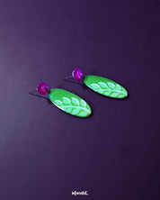 The Patbaan drop earrings featuring delicate hand-painted white leaf motifs on an oval green base, paired with bold pink studs for a lively, nature-inspired statement — Muselot.
