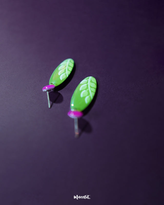A zoomed-in side view of the Patbaan drop earrings, highlighting the green leaf-shaped dangles paired with vibrant pink studs. The image showcases the textured finish and bold color contrast, reflecting the handcrafted charm and standout design perfect for playful yet elegant looks — Muselot.