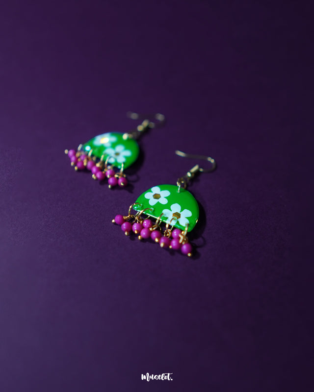 Phoolbaan floral hook earrings featuring bold white flowers painted on a glossy green surface, accented with delicate magenta bead drops—celebrating vibrant, handmade charm — Muselot.