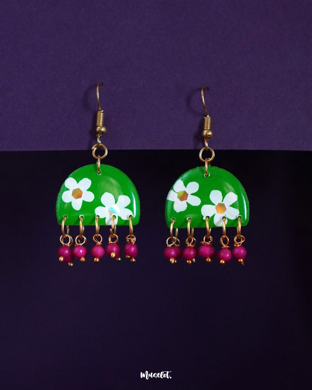 Phoolbaan hook earrings featuring a bright green base adorned with hand-painted white florals, finished with playful magenta bead danglers—showcasing cheerful charm and highlighting handcrafted artistry — Muselot.