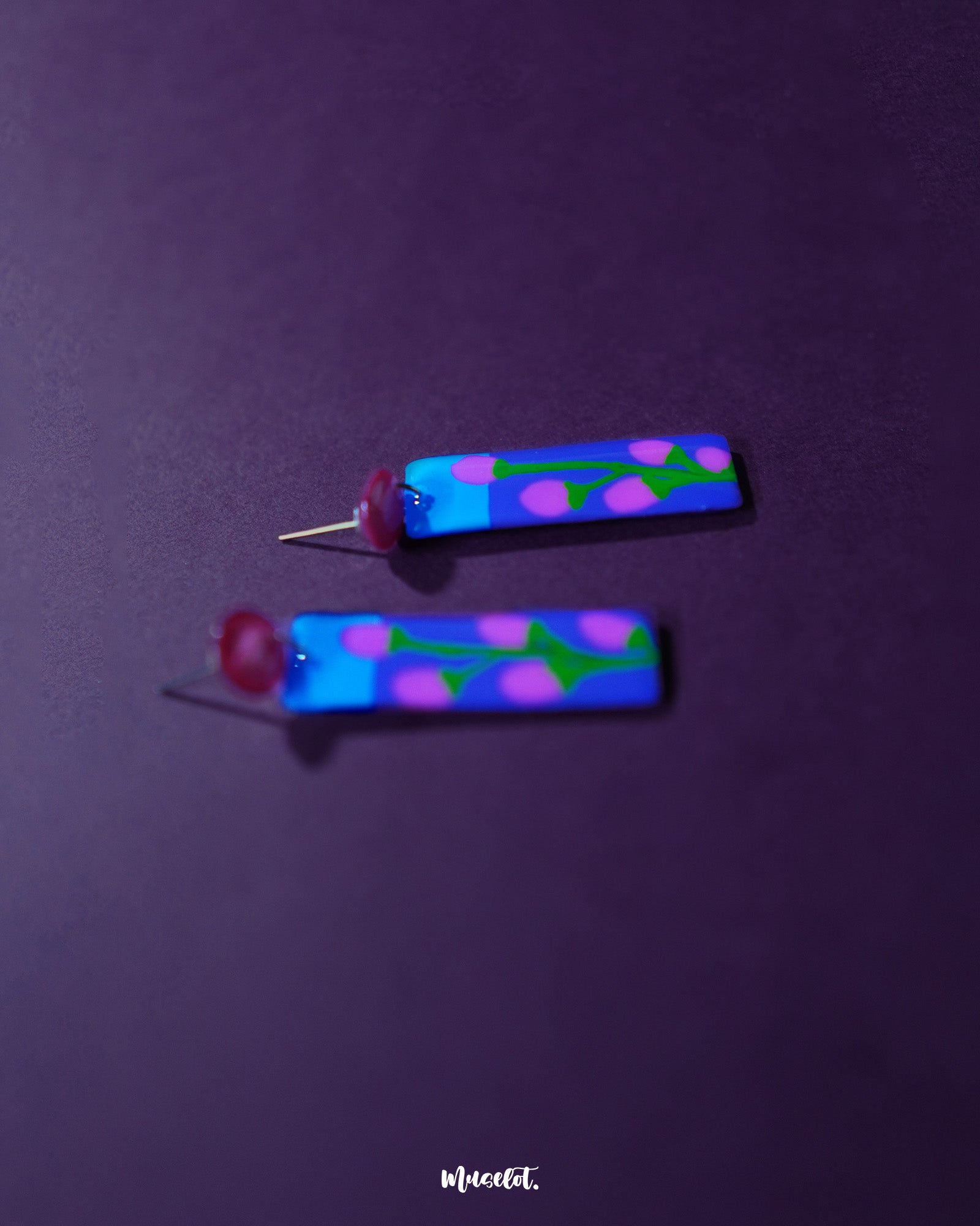 Close-up of Raatgul floral earrings showcasing the intricate hand-painted details—blush pink buds with green vines blossoming against a deep indigo backdrop, finished with glossy shine and bold red studs — Muselot.