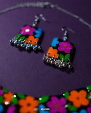 A close-up view of the Rangbaagh black floral earrings featuring delicate blue, orange, and purple flowers arranged in a balanced composition, paired with metallic gungroo drops that add a festive jingle and artisanal charm — Muselot