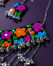A focused view of the title necklace from the Rangbaagh black floral set, featuring vibrant hand-painted blooms in blue, orange, and purple against a dark base, with layered metallic accents that showcase its boho-traditional fusion — Muselot