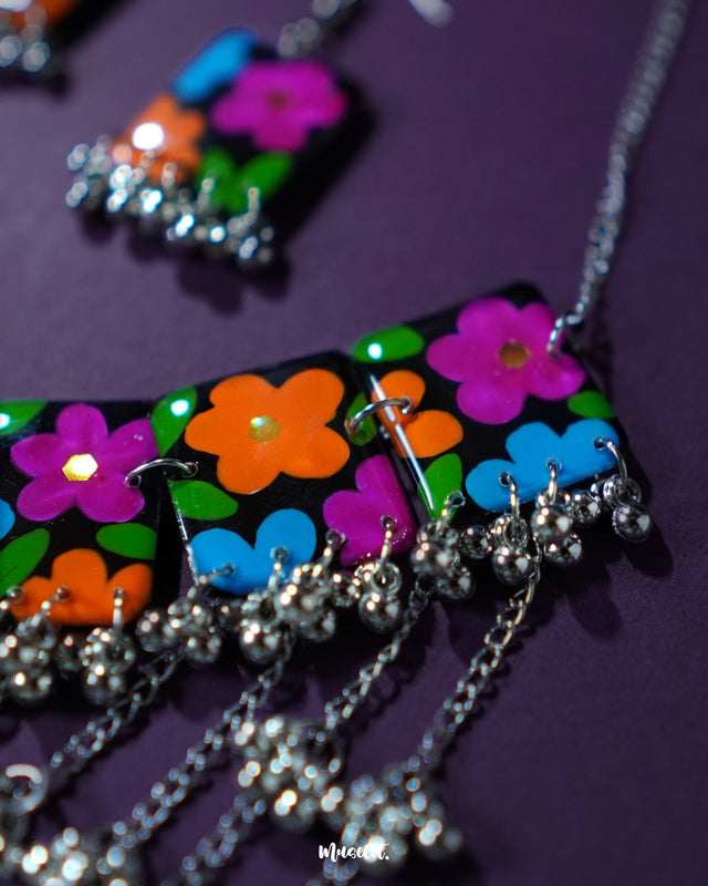 A focused view of the title necklace from the Rangbaagh black floral set, featuring vibrant hand-painted blooms in blue, orange, and purple against a dark base, with layered metallic accents that showcase its boho-traditional fusion — Muselot