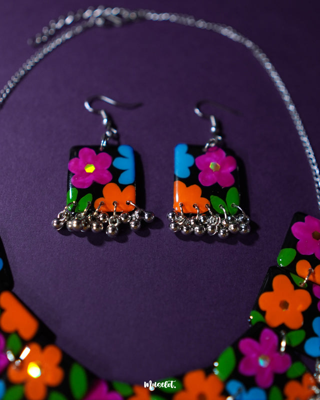 A vibrant shot of the earrings from the Rangbaagh black floral necklace set, showcasing blue, orange, and purple flower accents with silver gunghroo details, blending vivid color with artisanal elegance — Muselot.