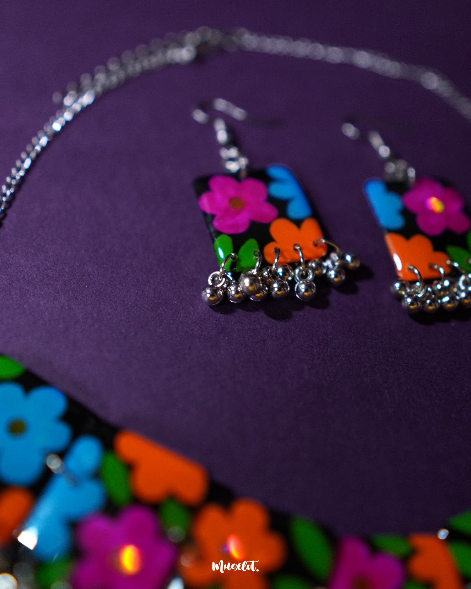 A close-up view of the Rangbaagh black floral earrings featuring delicately handcrafted blooms in vibrant blue, orange, and purple shades, paired with intricate silver detailing that brings a playful yet traditional charm — Muselot.