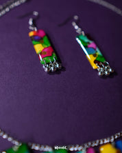 Colorful handcrafted jewelry set featuring a vibrant necklace and matching earrings with abstract multicolor patterns and silver bead accents, showcased on a deep purple background – Muselot.