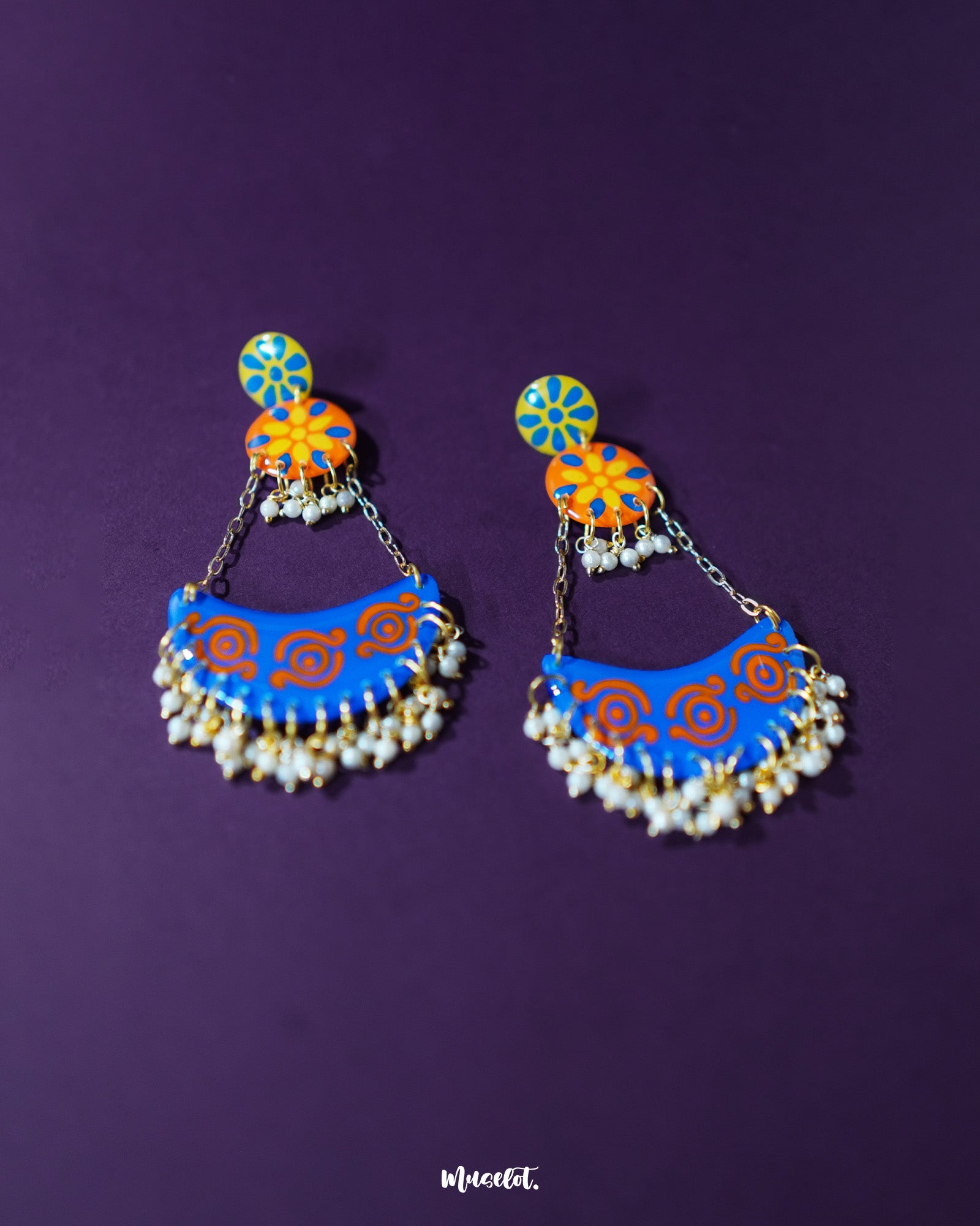 A detailed view of the Ranglahar blue chandbaali earrings showcasing the crescent-shaped design adorned with delicate pearl hangings, bold orange accents, and finely painted blue enamel—an elegant fusion of tradition and statement style — Muselot.