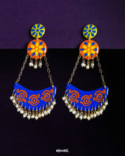 A vibrant pair of Ranglahar chandbali earrings featuring bold blue and orange crescent drops with intricate swirl patterns, suspended by golden chains from floral enamel tops, finished with tiny pearl danglers that add rhythmic charm and festive elegance — Muselot.