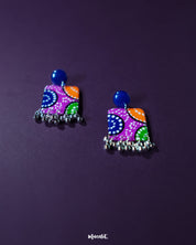 Rangras stud earrings displayed on a soft lavender-toned backdrop, highlighting their colorful hand-painted folk motifs and bold circular silhouette — a statement of vibrant artistry and culture — Muselot