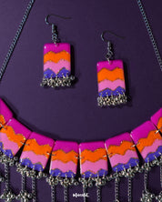 A pair of handcrafted earrings from the Rangrezan set rest against a purple background, showcasing their vivid beadwork and lively colors that mirror the joyful spirit of traditional Indian aesthetics — Muselot.