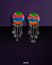 A vibrant pair of round handcrafted earrings featuring bold zigzag patterns in green, pink, blue, and orange, finished with dangling silver chains and clustered beads—bursting with festive charm and playful movement – Muselot.