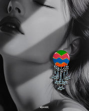 A close-up of a woman wearing the Rangtarang chain earrings, showcasing their vivid hand-painted round tops in green, pink, blue, and orange zigzags, with silver bead chains cascading down—capturing a joyful fusion of folk artistry and bold individuality – Muselot.
