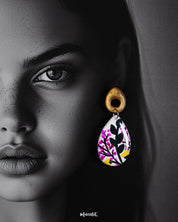 A close-up of a model wearing the Raushanbahaar handmade floral drop earrings, showcasing the teardrop design with vivid hand-painted pink and yellow flowers and lush green leaves, highlighting their detailed artistry and bold statement charm — Muselot.