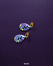 Raushanbahaar floral drop earrings laid against a soft neutral background, featuring a teardrop silhouette with delicate pink and yellow floral artwork and leafy details, highlighting the lively hand-painted charm and showcasing the beauty of handcrafted accessories — Muselot.