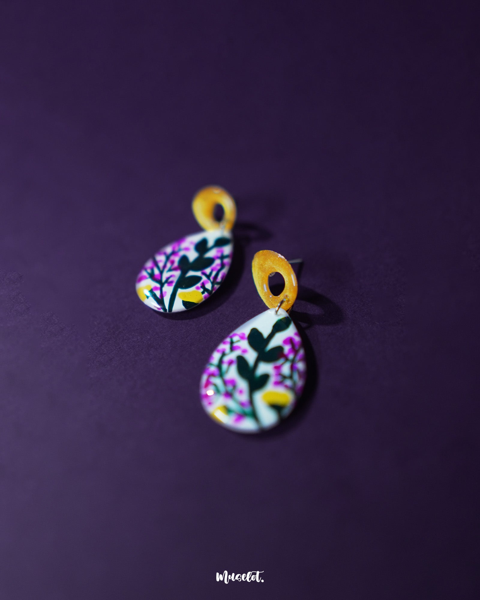 Close-up of Raushanbahaar floral drop earrings, capturing the teardrop shape adorned with pink and yellow hand-painted flowers and leafy accents, highlighting vibrant artistry and showcasing the intricacy of handmade design — Muselot.