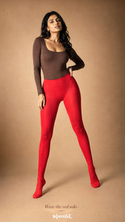 The model wears bright red opaque full-length stockings, showcasing their smooth finish, even colour coverage and closed-toe design – Muselot.