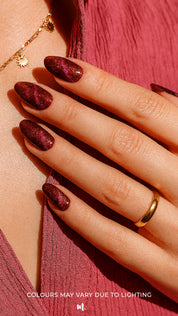 A model hand wearing Romantic Ruby Maroon Cat Eye Nail Art Stickers, showcasing a deep maroon-red base with a shimmering cat-eye effect that reflects light for a dazzling magnetic shine, adding a bold and glamorous finish – Muselot.