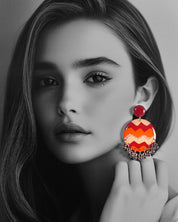 A model wearing the Sahar hook earrings, where the vivid maroon, orange, and mustard waves pop boldly against the dark backdrop, while the playful silver ghungroos add a rhythmic charm to the handcrafted design — Muselot.