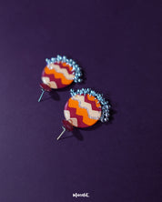 Sahar traditional stud earrings rest elegantly against a deep purple backdrop, showcasing their bold round form painted with maroon, orange, and mustard waves, finished with delicate silver ghungroos that lend a festive, handcrafted touch — Muselot.