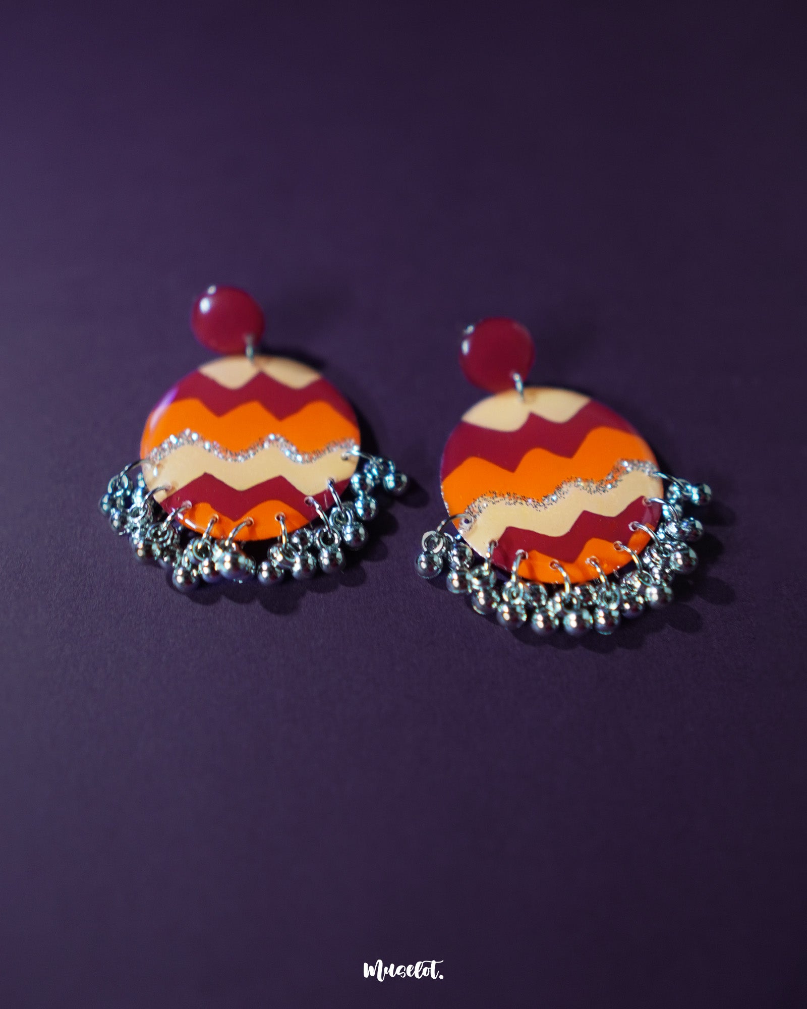 Flat lay of the Sahar traditional stud earrings highlighting the mustard and rust hues with oxidized silver-tone borders and dangling ghungroos that add a rustic, folk-inspired elegance — Muselot.