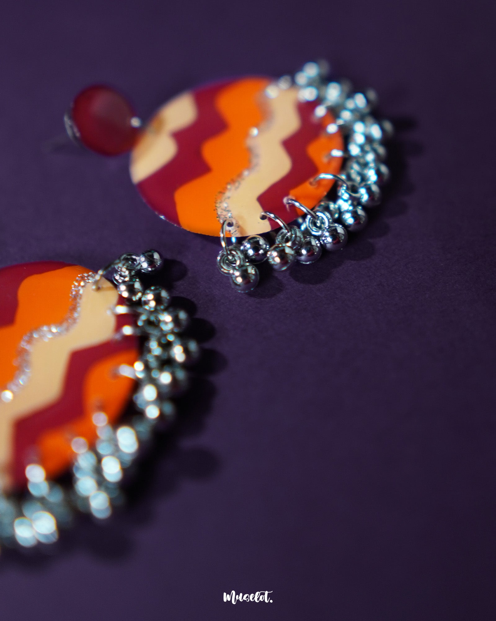 Close-up of the Sahar traditional stud earrings placed on a textured surface, showcasing their vibrant mustard and rust tones with ornate oxidized silver detailing and delicate ghungroo accents — Muselot.