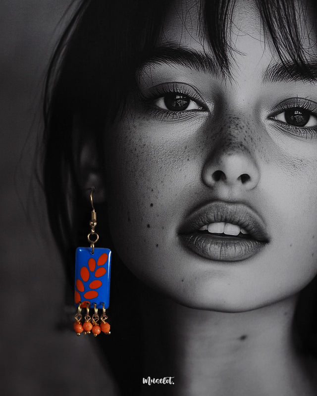 Closeup of a model wearing the Sandhyaraag boho drop earrings, highlighting the striking orange petal motifs on a blue base and showcasing the playful elegance of the dangling orange beads — Muselot.