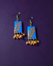 Sandhyaraag hook floral earrings placed on a purple background, featuring a bold blue base adorned with orange floral motifs and playful dangling beads that add a touch of boho flair — Muselot